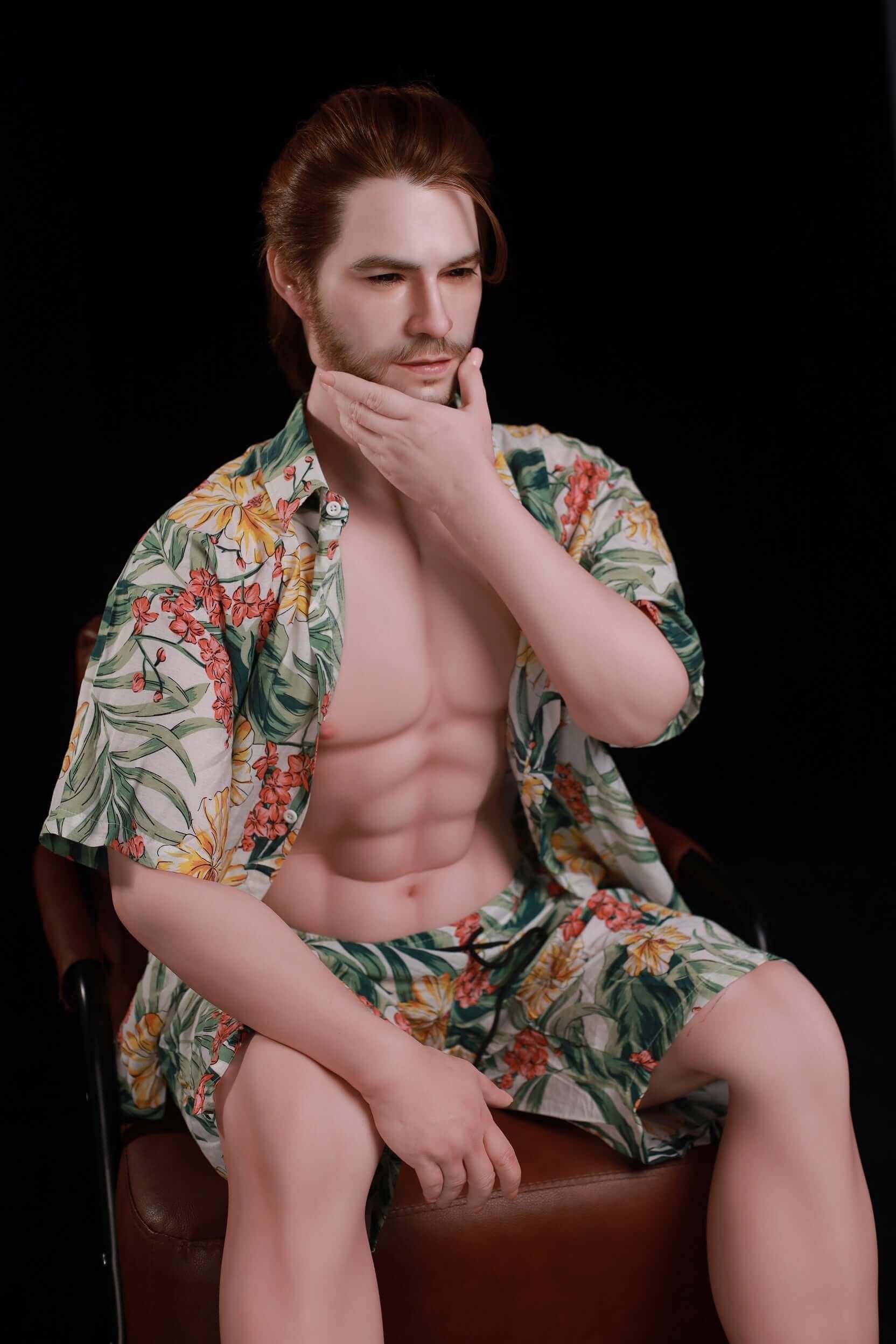 160cm Mason male silicone doll seated on brown leather stool, hand to chin, swept-back auburn hair with stubble goatee, open Hawaiian shirt revealing six-pack abs